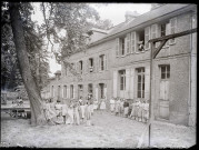 Enfants et sœurs à cornettes dans la cour d'une école de campagne.