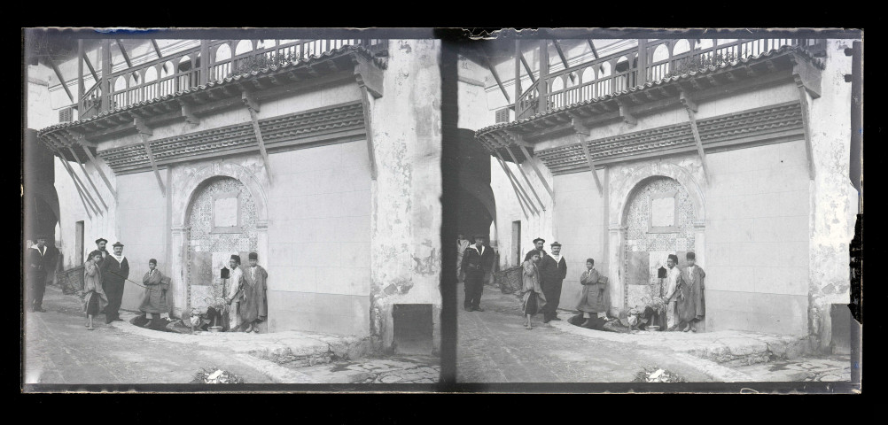 Bédouins à la fontaine et marins français dans les ruelles d'un souk en Algérie.