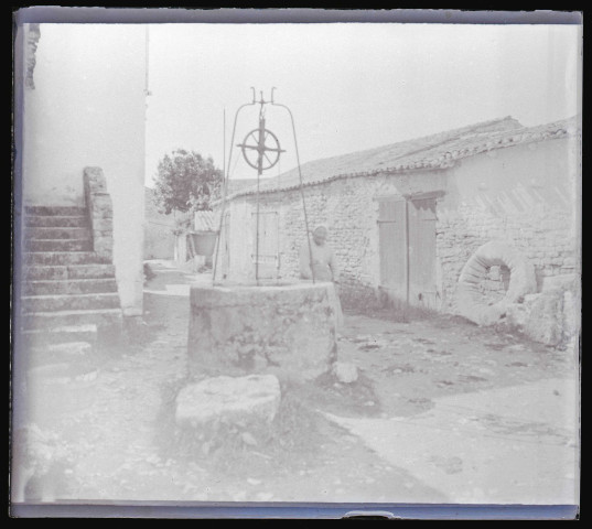 Vieille femme appuyée sur la margelle d'un puits dans un village de la campagne de Charente-Maritime.